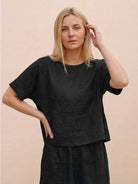 woman wearing black loose fit co-ord set with relaxed short sleeves and wide-leg pants against neutral background