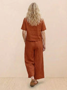 Woman wearing rust brown loose fit co-ord set with wide-leg pants and short-sleeve top, back view.
