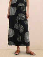 Black wide-leg pants with large gray circular prints, part of a loose fit co-ord set paired with brown slide sandals.