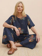 Woman wearing navy floral loose fit co-ord set with wide-leg pants and short-sleeve top sitting on woven rug with brown sandals