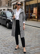 Woman wearing grey oversized Rain Couture Windbreaker with hood, black pants, white shirt, and sunglasses, holding coffee on city street.