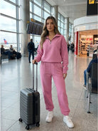 Woman wearing ultra-soft and comfy co-ord tracksuit set in pink at airport with suitcase