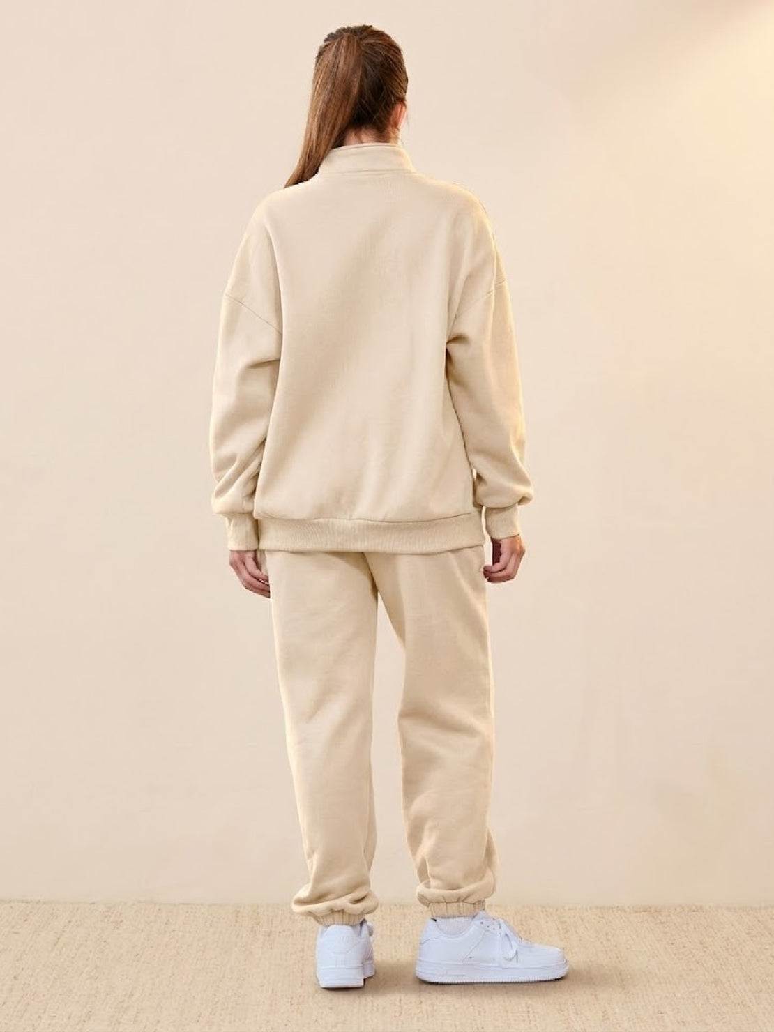 Back view of a person wearing beige ultra-soft and comfy co-ord tracksuit set with white sneakers on neutral background