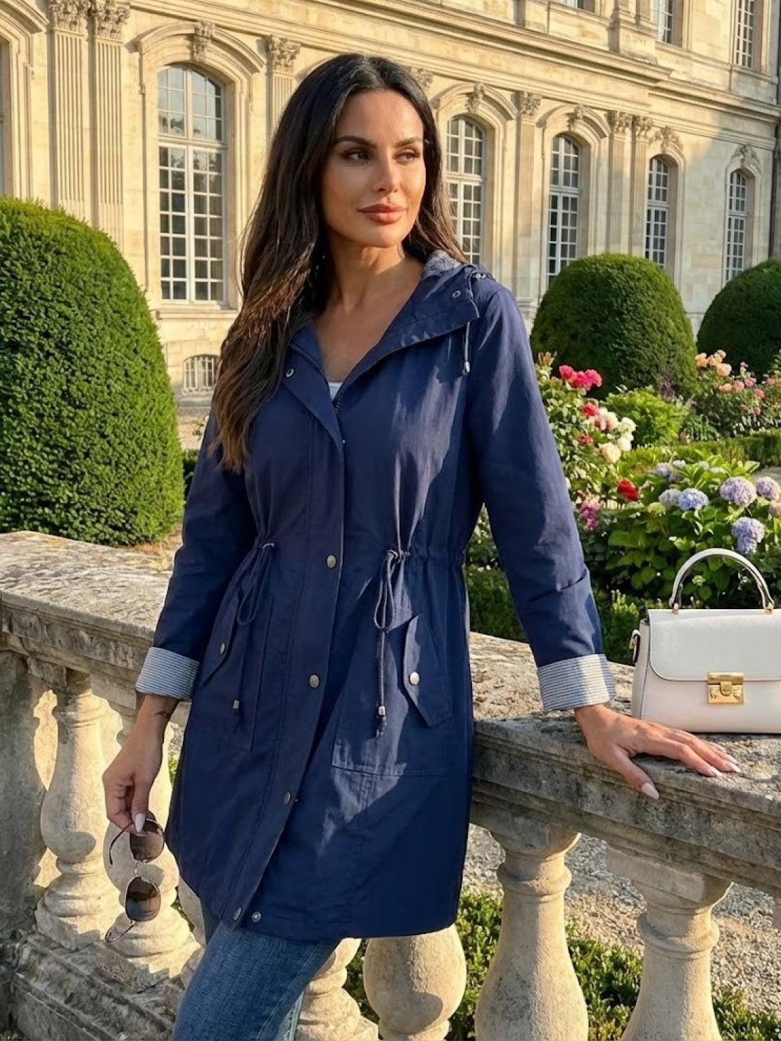 Women wearing navy blue water resistant windbreaker jacket with hood outdoors by garden and historic building